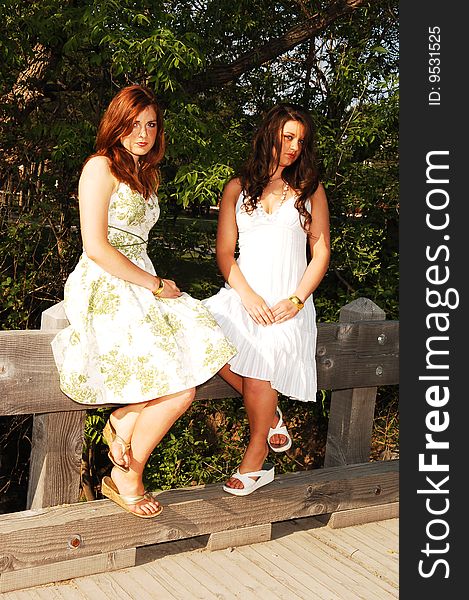 Two very pretty sisters sitting on the railing of a bridge in nice summer dresses, but looking quit sad. Two very pretty sisters sitting on the railing of a bridge in nice summer dresses, but looking quit sad.