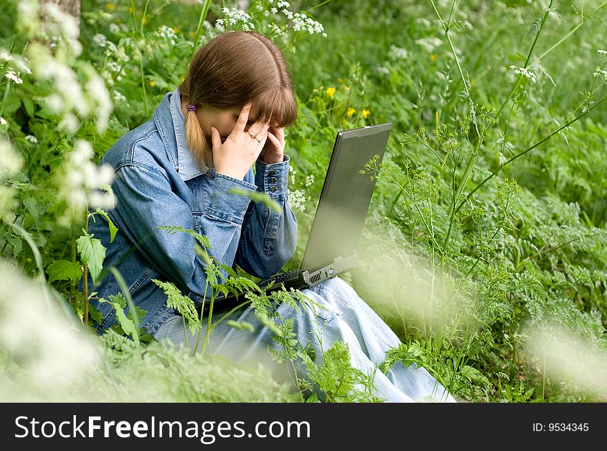 The beautiful girl with the laptop in park sits in a green grass. The beautiful girl with the laptop in park sits in a green grass