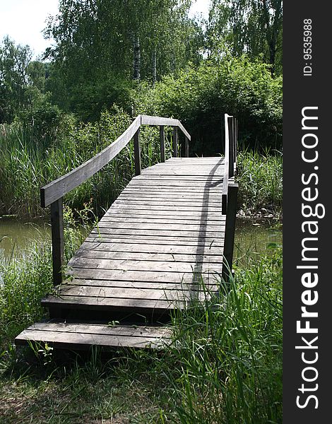 Bridge of wooden planks leads over small river. Bridge of wooden planks leads over small river