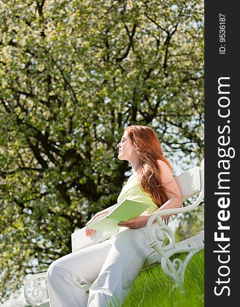 Red hair woman sitting on white bench in summer meadow; shallow DOF. Red hair woman sitting on white bench in summer meadow; shallow DOF