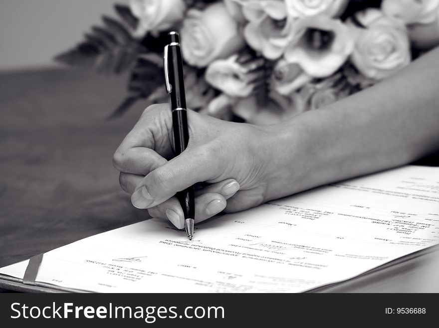 Woman's hand signing documents near a wedding bouquet. Woman's hand signing documents near a wedding bouquet