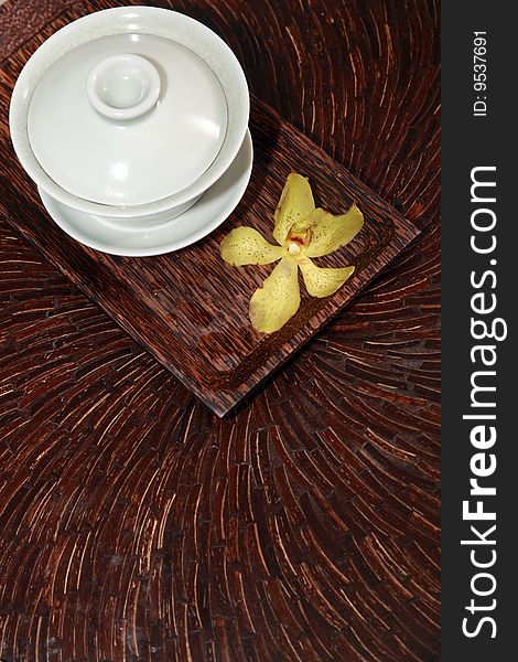 A Chinese style tea cup and orchid are placed on the dark wooden carved table