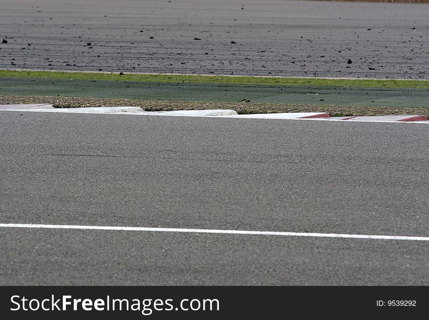 Sawtooth kerbs at a motorsport circuit. Smooth tarmac provides a large single colour area ideal for a background. Sawtooth kerbs run across the centre of the image with the focus, above them is run-off area littered with rubber debris from tyres. Sawtooth kerbs at a motorsport circuit. Smooth tarmac provides a large single colour area ideal for a background. Sawtooth kerbs run across the centre of the image with the focus, above them is run-off area littered with rubber debris from tyres.