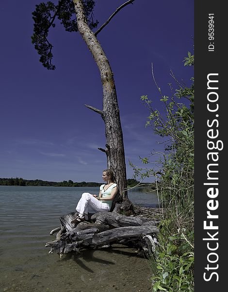 Blonde female leaning against a tree and enjoying the beautiful nature around her. Blonde female leaning against a tree and enjoying the beautiful nature around her