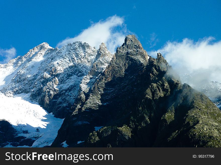 Snow covered mountain peaks with clouds against blue skies on sunny day. Snow covered mountain peaks with clouds against blue skies on sunny day.
