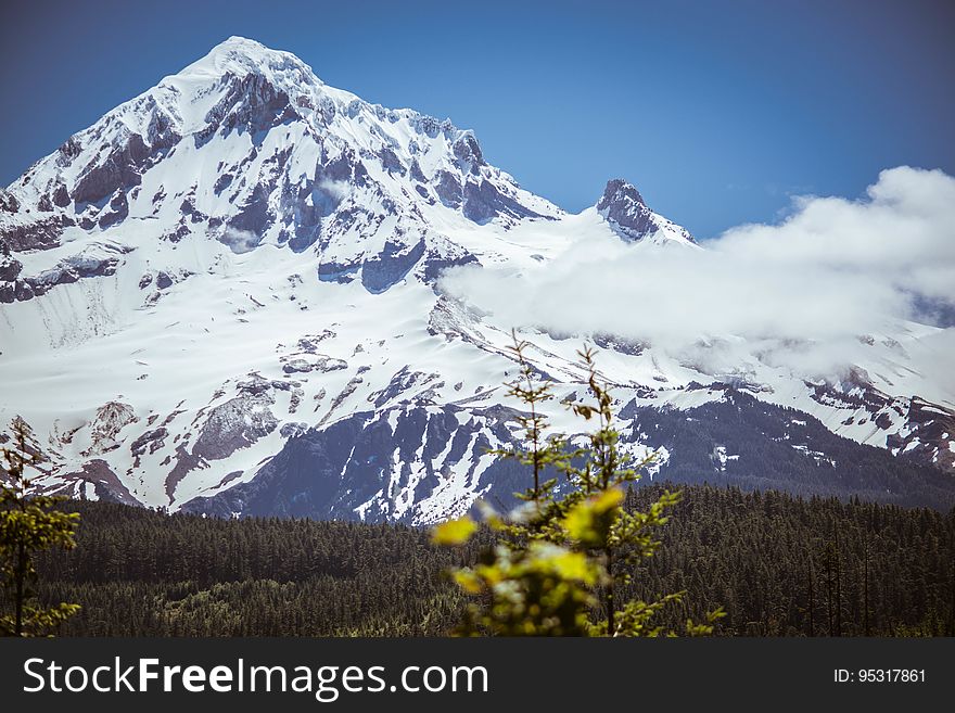 Landscape with snow covered mountain peak surrounded with clouds on sunny day against blue skies.