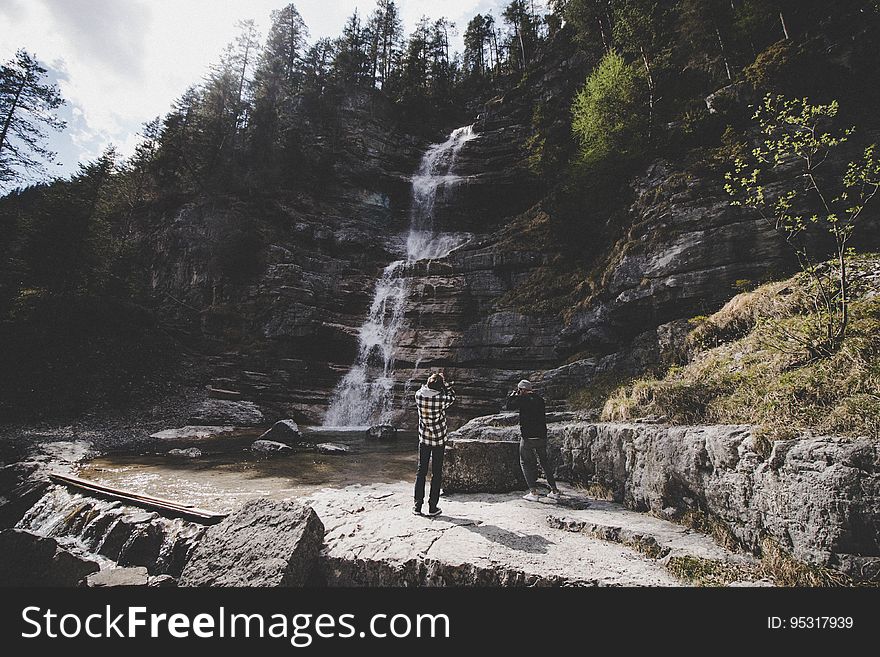 Hikers standing next to waterfall along hillside in forest. Hikers standing next to waterfall along hillside in forest.