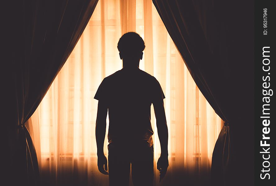 Silhouette of young boy standing in front of curtains on interior window. Silhouette of young boy standing in front of curtains on interior window.