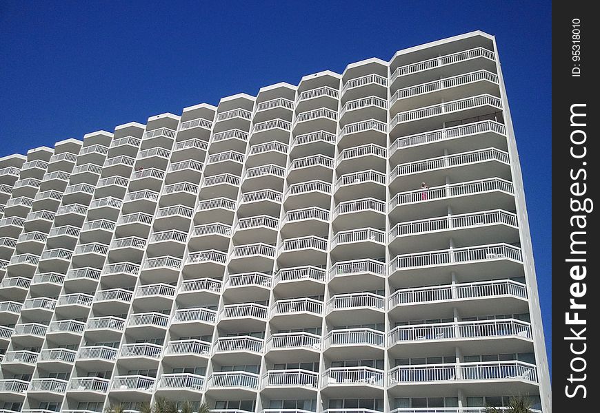Balconies on exterior of modern apartment building against blue skies on sunny day.