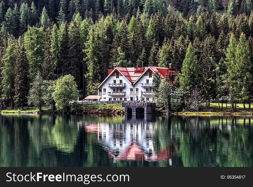 A chalet on the lake coast reflecting on the water surface and an evergreen forest in the background. A chalet on the lake coast reflecting on the water surface and an evergreen forest in the background.