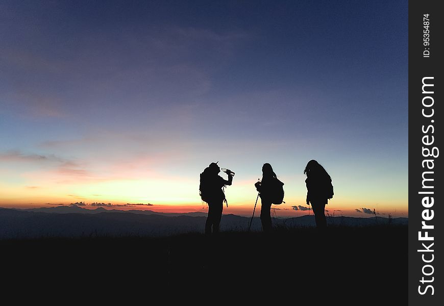 The silhouettes of three people standing on a mountain at sunset. The silhouettes of three people standing on a mountain at sunset.