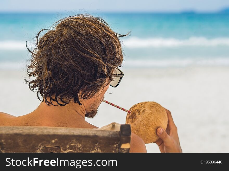 Young man drinking coconut milk on Chaise-longue on beach.