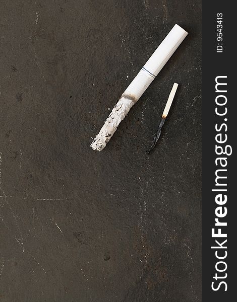 Smoking cigarette and burned match lying on metal dark background. Smoking cigarette and burned match lying on metal dark background