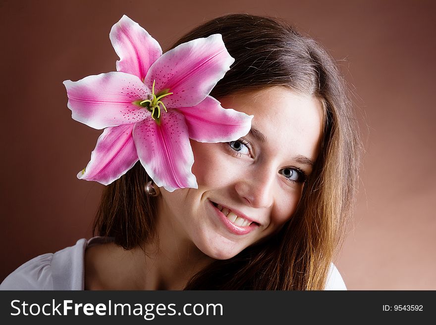 A pretty young woman with long brown hair posing with a pink lilynear her face. A pretty young woman with long brown hair posing with a pink lilynear her face