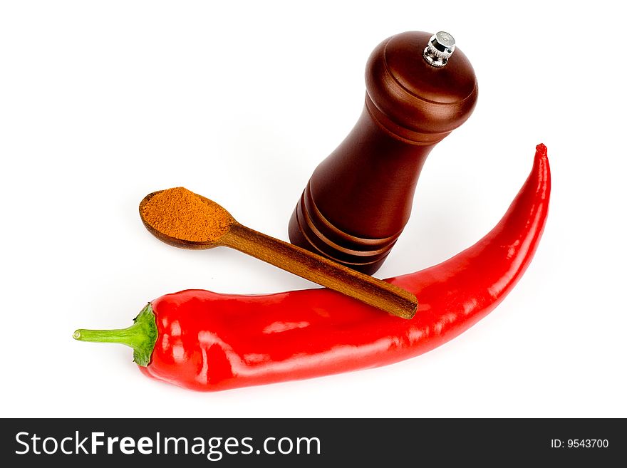 A composition of a pod of red chile pepper , a wooden hand mill for a grinding and a wooden spoonful of red ground pepper on a white background. A composition of a pod of red chile pepper , a wooden hand mill for a grinding and a wooden spoonful of red ground pepper on a white background