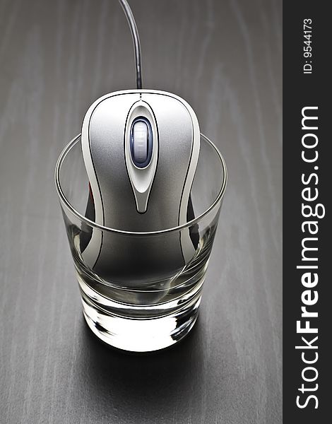 Metallic computer mouse in a glass tumbler on black