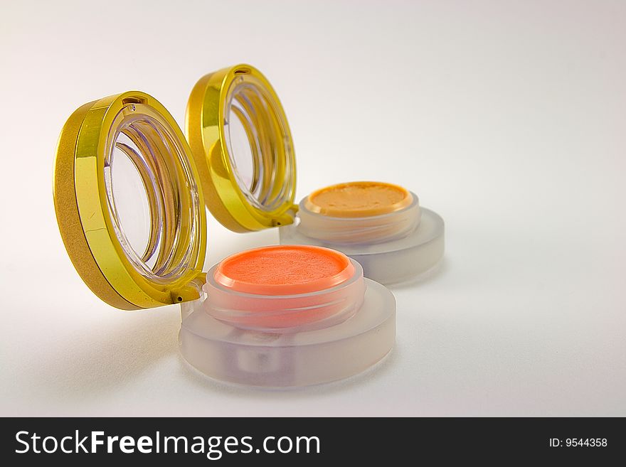 Two lipstick pots with lids open on a plain background