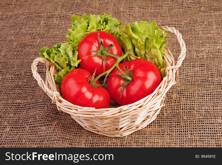 Bunch of three red tomatoes and lettuce in basket on rough linen fabric.