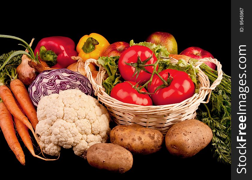 Pile of various vegetables. Isolated on black. Three tomatoes in basket, carrots, paprika, potatoes, onions.