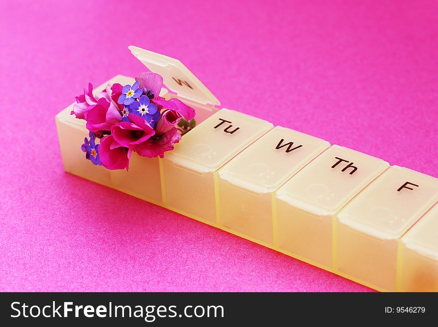 A seven day pill dispenser with small fresh flowers popping out of it. A seven day pill dispenser with small fresh flowers popping out of it