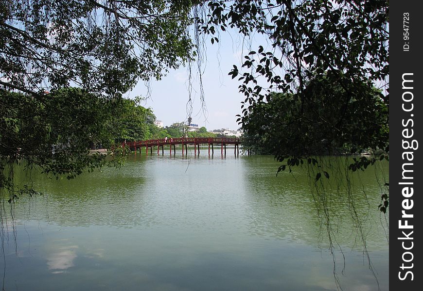 Photo of a red bridge that crosses part of a lake in central hanoi to an island with a pagoda that overlooks the lake.