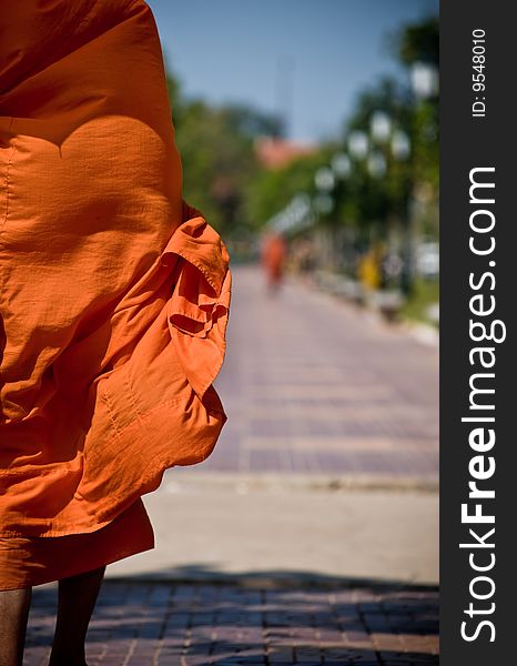 A monk walks the streets in asia, the wind blowing his loosely fitting robe. the vibrant orange color stands out nicely in the urban setting. shadow of his umbrella can be seen on his shoulders showing that he is keeping cool under the hot asian sun. A monk walks the streets in asia, the wind blowing his loosely fitting robe. the vibrant orange color stands out nicely in the urban setting. shadow of his umbrella can be seen on his shoulders showing that he is keeping cool under the hot asian sun.