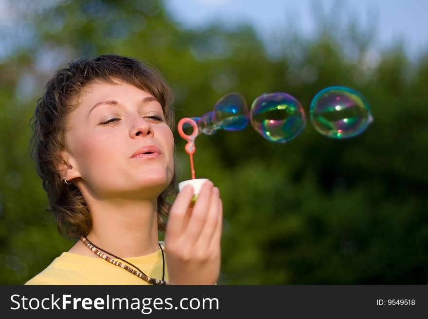 A young woman blowing up soap-bubbles on the green trees background. A young woman blowing up soap-bubbles on the green trees background