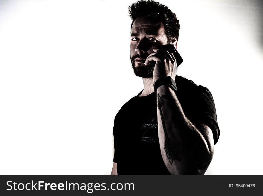 Dark bearded man with shock of black hair, black jumper and tattoo using mobile phone and looking distressed or disturbed by the message, white background. Dark bearded man with shock of black hair, black jumper and tattoo using mobile phone and looking distressed or disturbed by the message, white background.