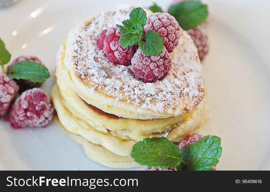 A plate of pancakes with raspberries and mint leaves on top. A plate of pancakes with raspberries and mint leaves on top.