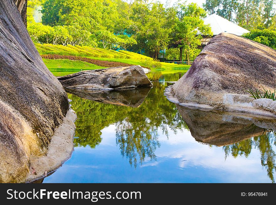 Scenic view of green trees and large boulders reflecting on lake in park, summer scene. Scenic view of green trees and large boulders reflecting on lake in park, summer scene.