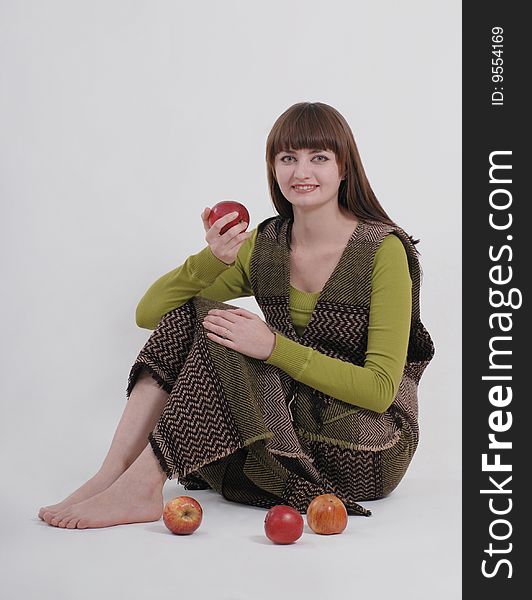 A girl is sitting on the floor, and holding an apple (three more apples are lying nearby). A girl is sitting on the floor, and holding an apple (three more apples are lying nearby)