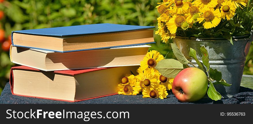 A stack of books on a table with an apple. A stack of books on a table with an apple.