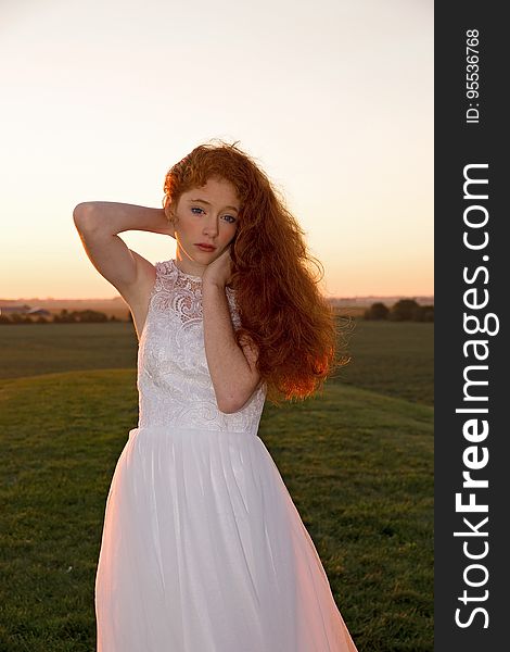 A woman standing on a field wearing a white dress at sunset. A woman standing on a field wearing a white dress at sunset.