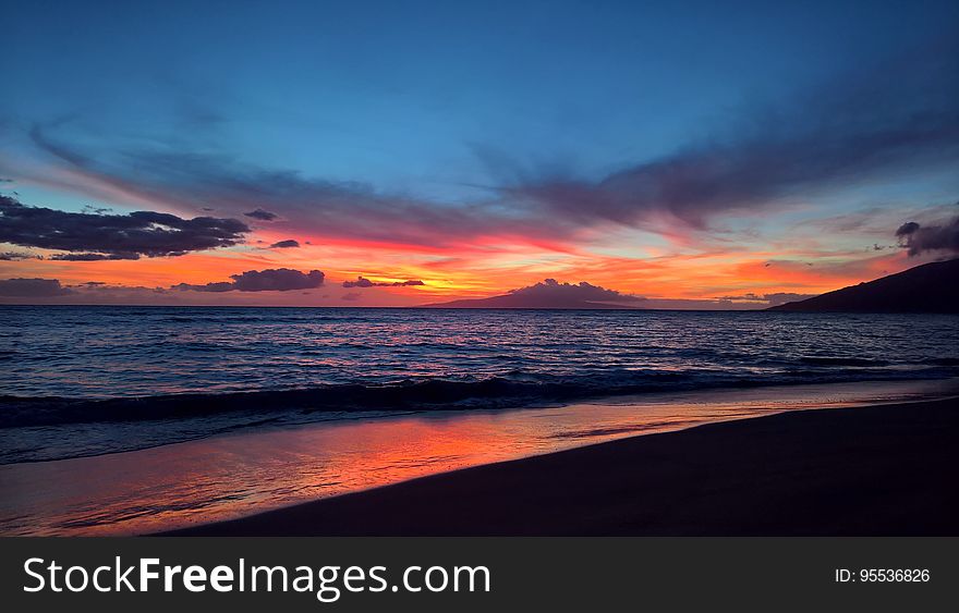 Sunset over beach waterfront with blue skies.