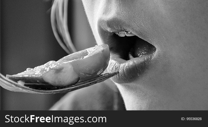 Close up of girl with braces eating piece of food from fork in black and white. Close up of girl with braces eating piece of food from fork in black and white.