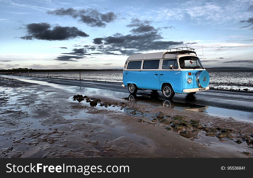 A blue retro campervan driving along a muddy beach at dusk. A blue retro campervan driving along a muddy beach at dusk.