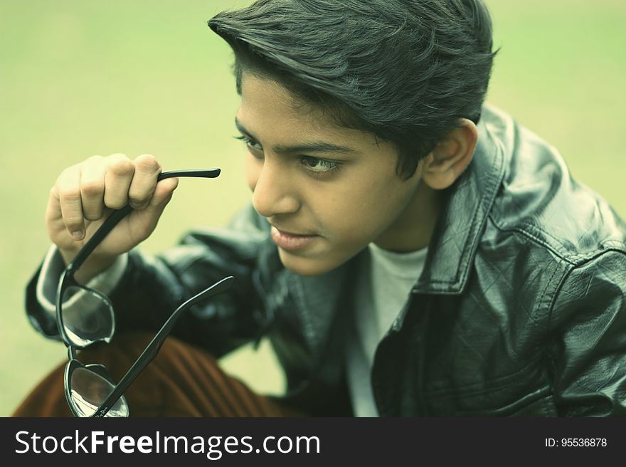 Young boy with serious expression holding glasses in portrait. Young boy with serious expression holding glasses in portrait.