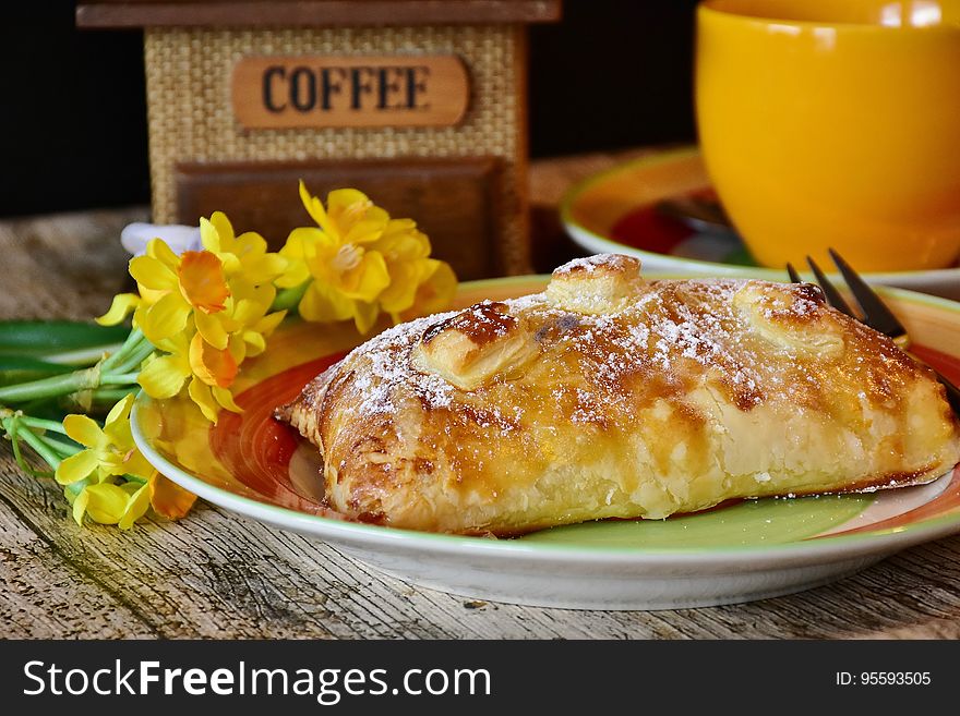 Baked puff pastry and fork on plate with daffodils next to yellow coffee cup. Baked puff pastry and fork on plate with daffodils next to yellow coffee cup.