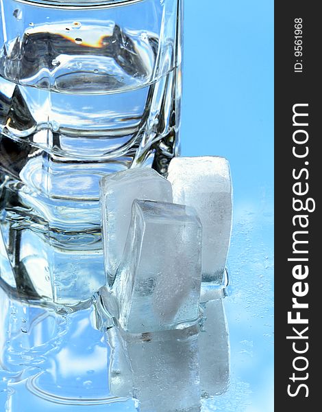 Ice cubes lying near glass of water on background with blue sky. Ice cubes lying near glass of water on background with blue sky