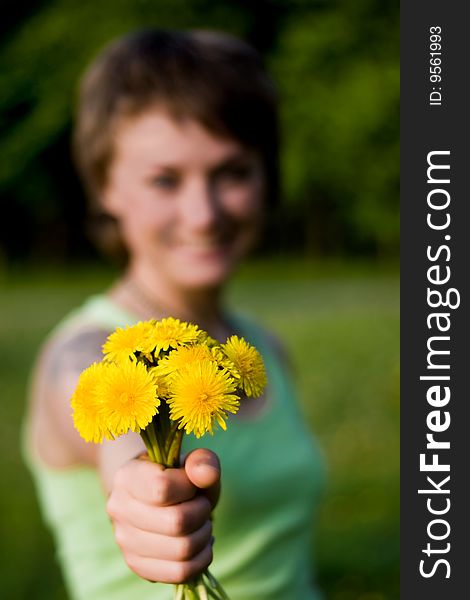 A young cheerful woman with a bunch of dandelions in her hand