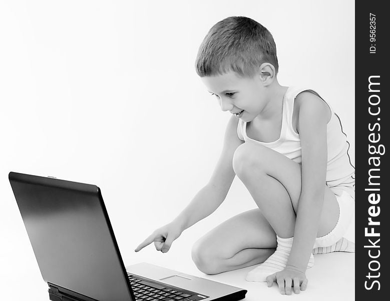 The little boy in a vest sits on a floor and looks on laptop. The little boy in a vest sits on a floor and looks on laptop