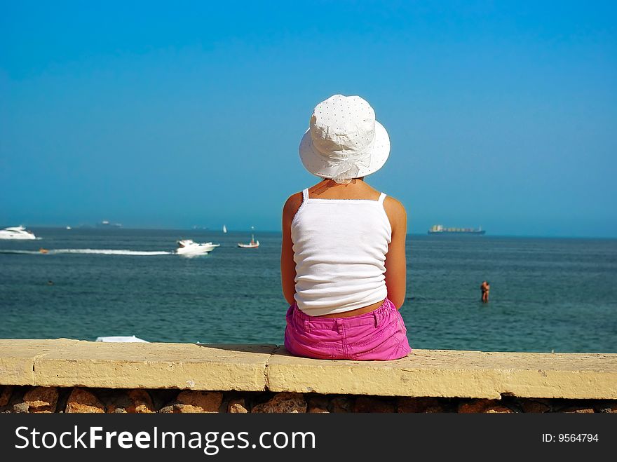 Girl is sitting on a border of the beach and looking at the horizon. Girl is sitting on a border of the beach and looking at the horizon