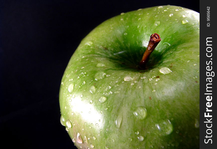 A granny smith apple with water drops on a black background. A granny smith apple with water drops on a black background