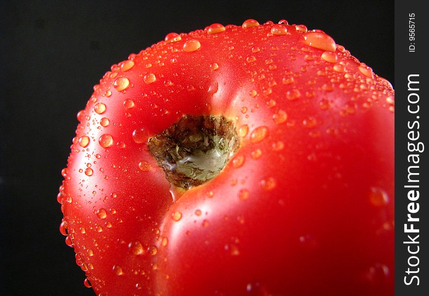 A fresh tomato with water drops on a black background