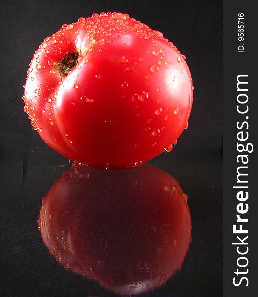 A fresh tomato with water drops on a black background