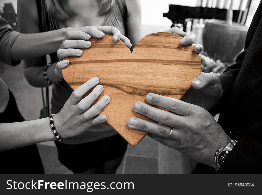 Desaturated hands holding wooden heart.