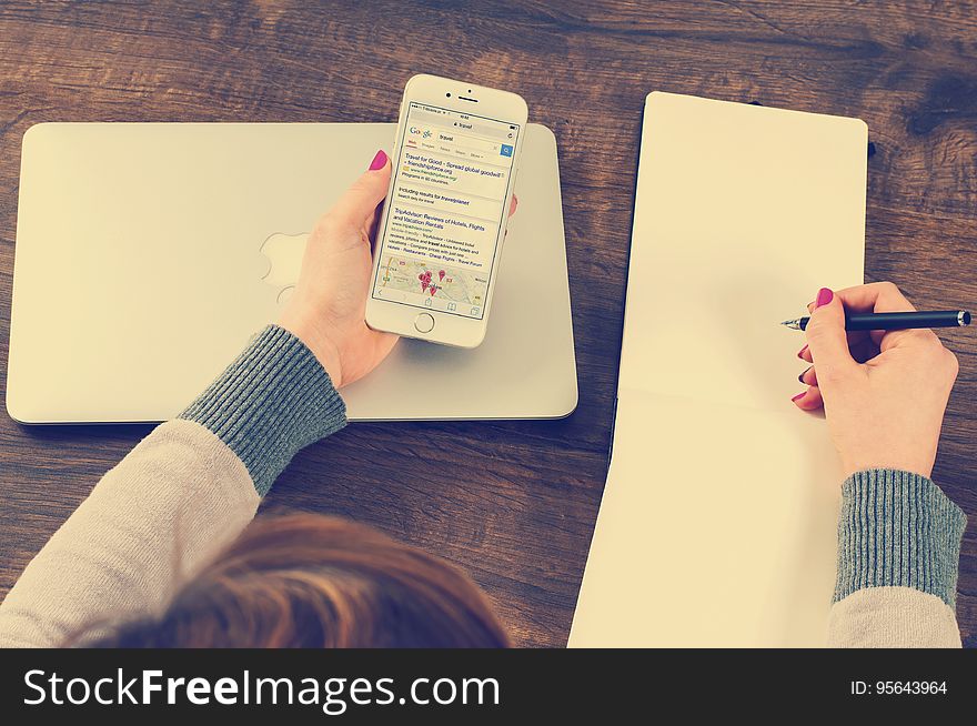 Overhead of woman holding cellphone in one hand and pen over blank notebook on in other on wooden desktop with computer. Overhead of woman holding cellphone in one hand and pen over blank notebook on in other on wooden desktop with computer.