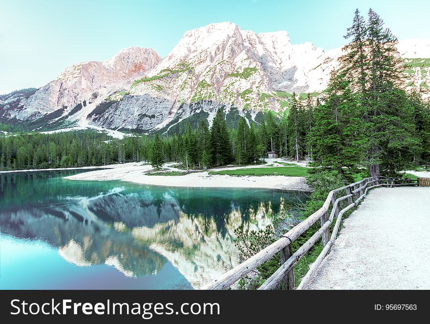 Mountains reflecting in calm waters of alpine lake with bridge and pine trees along banks. Mountains reflecting in calm waters of alpine lake with bridge and pine trees along banks.