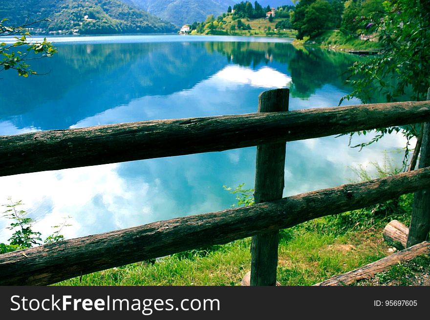 A wooden fence on the lake coast and hills and clouds reflecting on the water surface in the background. A wooden fence on the lake coast and hills and clouds reflecting on the water surface in the background.