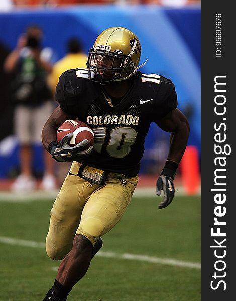 Closeup of a college player on the Colorado team running at an angle during a game with the football cradled in his right arm. Closeup of a college player on the Colorado team running at an angle during a game with the football cradled in his right arm.